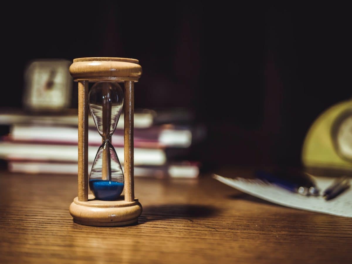 An hourglass with blue sand on desk signifying how long does divorce take after filing papers in Australia